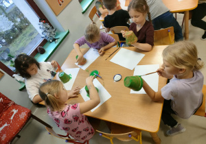 "Pszczółki" majują zieloną farbą małą doniczkę.