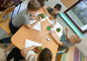 "Pszczółki" majują zieloną farbą małą doniczkę.