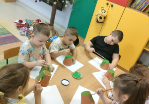 "Pszczółki" majują zieloną farbą małą doniczkę.