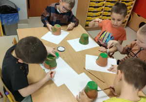 "Pszczółki" majują zieloną farbą małą doniczkę.