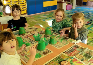 "Motylki" malują zieloną farbą małą doniczkę.