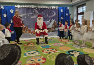 Wizyta Świętego Mikołaja w grupie "Wiewiórek". Mikołaj siedzi na krzesełku, natomiast dzieci stoją w półkolu.