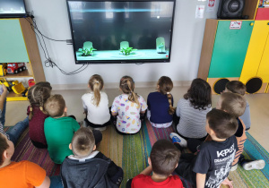 Dzieci oglądają film edukacyjny o rukoli na ekranie multimedialnym.