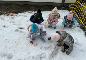 Kilkoro dzieci z grupy "Żabek" maluje śnieg za pomocą farby i pędzelków.
