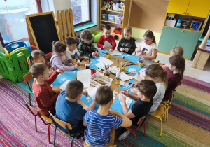 Dzieci siedzą przy połączonych stołach i wykonują pracę plastyczną pt. "Rodzina bałwanków" wg instrukcji nauczyciela.
