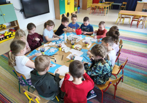 Dzieci siedzą przy połączonych stołach i wykonują pracę plastyczną pt. "Rodzina bałwanków" wg instrukcji nauczyciela.