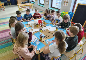 Dzieci siedzą przy połączonych stołach i wykonują pracę plastyczną pt. "Rodzina bałwanków" wg instrukcji nauczyciela.