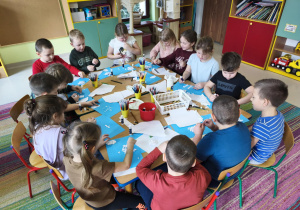 Dzieci siedzą przy połączonych stołach i wykonują pracę plastyczną pt. "Rodzina bałwanków" wg instrukcji nauczyciela.