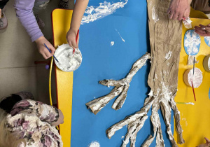 Dzieci malują drzewo z wykorzystaniem przygotowanej farby.