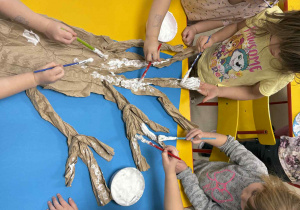 Dzieci malują drzewo z wykorzystaniem przygotowanej farby.