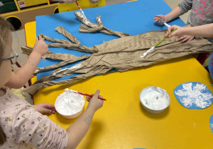 Dzieci malują drzewo z wykorzystaniem przygotowanej farby.