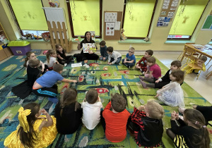 Dzieci z grupy "Motylków" słuchają nauczycielki, która omawia publikację pt. "Skąd się biorą produkty ekologiczne?"