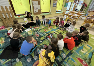 Dzieci z grupy "Motylków" słuchają nauczycielki, która omawia publikację pt. "Skąd się biorą produkty ekologiczne?"