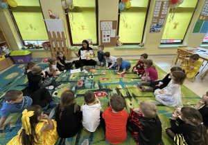 Dzieci z grupy "Motylków" słuchają nauczycielki, która omawia publikację pt. "Skąd się biorą produkty ekologiczne?"