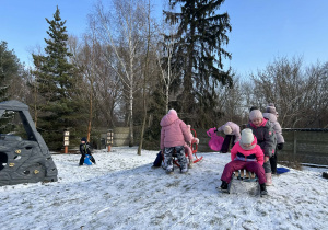 "Motylki" zjeżdżają na saneczkach/jabłuszkach na przedszkolnym placu zabaw.