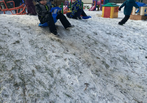 "Motylki" zjeżdżają na saneczkach/jabłuszkach na przedszkolnym placu zabaw.