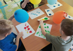 Kilkoro dzieci z grupy "Motylków", korzystając z kolorowych farb i balonów tworzy pracę plastyczną.