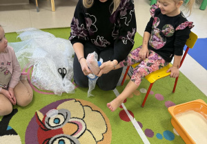 Nauczycielka owija stopy dziewczynki folią bąbelkową.