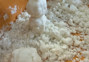 Dzieci lepią bałwanki ze sztucznego śniegu.