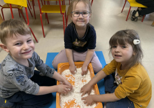 Dzieci lepią bałwanki ze sztucznego śniegu.