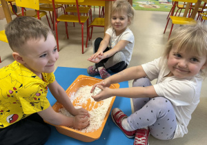 Dzieci lepią bałwanki ze sztucznego śniegu.