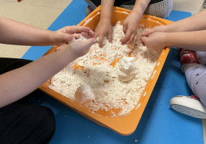 Dzieci lepią bałwanki ze sztucznego śniegu.