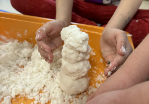 Dzieci lepią bałwanki ze sztucznego śniegu.