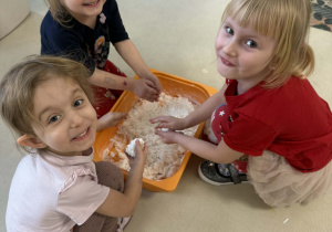 Dzieci lepią bałwanki ze sztucznego śniegu.