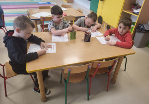 Kilkoro dzieci przy stoliku rozwiązuje tematyczną kartę pracy.