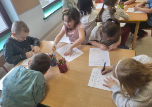 Kilkoro dzieci przy stoliku rozwiązuje tematyczną kartę pracy.