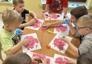 Kilkoro dzieci z grupy "Motylków" przy stole bawi się piaskiem kinetycznym.