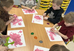 Kilkoro dzieci z grupy "Motylków" przy stole bawi się piaskiem kinetycznym.