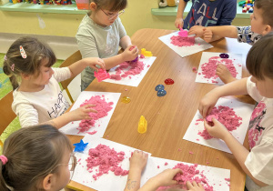 Kilkoro dzieci z grupy "Motylków" przy stole bawi się piaskiem kinetycznym.