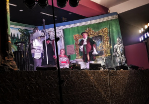 Przebrani aktorzy na scenie pełnej dekoracji.