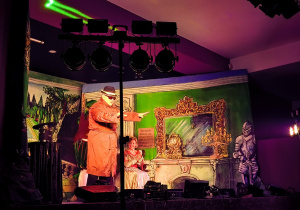 Przebrani aktorzy na scenie pełnej dekoracji.