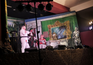 Przebrani aktorzy na scenie pełnej dekoracji.