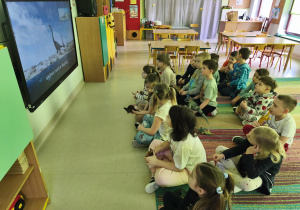 Dzieci oglądają film edukacyjny o dinozaurach na ekranie multimedialnym.