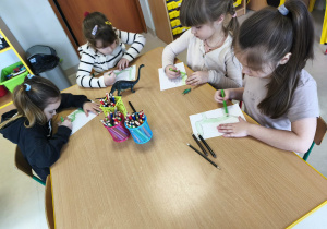 Kilkoro dzieci przy stoliku samodzielnie rysuje swojego dinozaura.