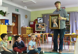 Pan Paweł prezentuje dzieciom swe obrazy. Na tym zdjęciu trzyma w dłoniach obraz przedstawiający Karolinkę w wieku 3 lat.