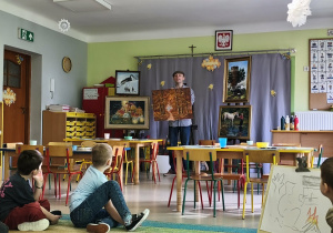 Pan Paweł prezentuje dzieciom swe obrazy. Na tym zdjęciu trzyma w dłoniach obraz przedstawiający złotą jesień.
