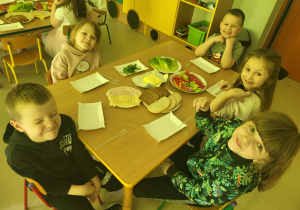 Kilkoro dzieci przy stole gotowych do przygotowania zdrowych, kolorowych kanapek.