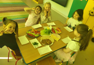 Kilkoro dzieci przy stole gotowych do przygotowania zdrowych, kolorowych kanapek.