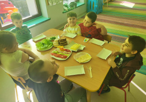 Kilkoro dzieci przy stole gotowych do przygotowania zdrowych, kolorowych kanapek.