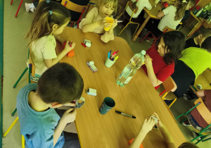 Kilkoro dzieci przy stoliku ozdabia wybrany przez siebie kubek według własnego uznania.