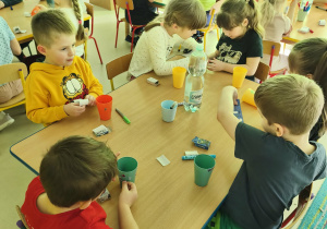 Kilkoro dzieci przy stoliku ozdabia wybrany przez siebie kubek według własnego uznania.