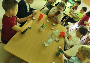 Kilkoro dzieci przy stoliku ozdabia wybrany przez siebie kubek według własnego uznania.