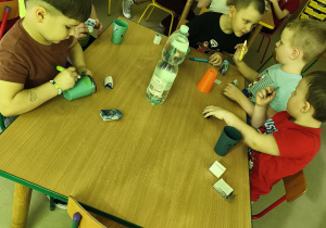 Kilkoro dzieci przy stoliku ozdabia wybrany przez siebie kubek według własnego uznania.