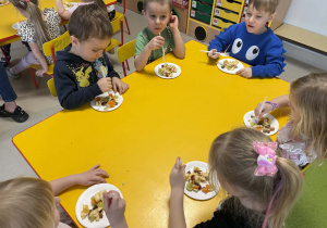 Dzieci jedzą przygotowana przez siebie sałatkę owocową.