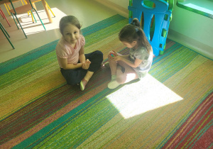 Dzieci siedząc na dywanie, przeglądają sie w małych lusterkach.