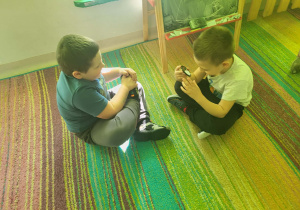 Dzieci siedząc na dywanie, przeglądają sie w małych lusterkach.